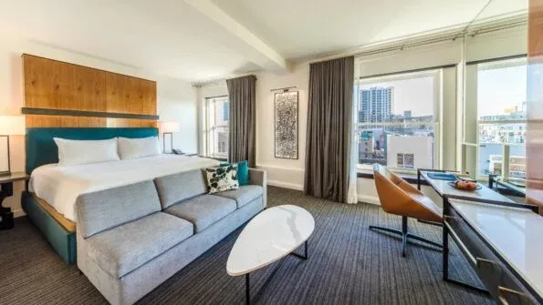 A king room with coastal grey colors, view of downtown and a pop of turquoise around the bed at Andaz San Diego.