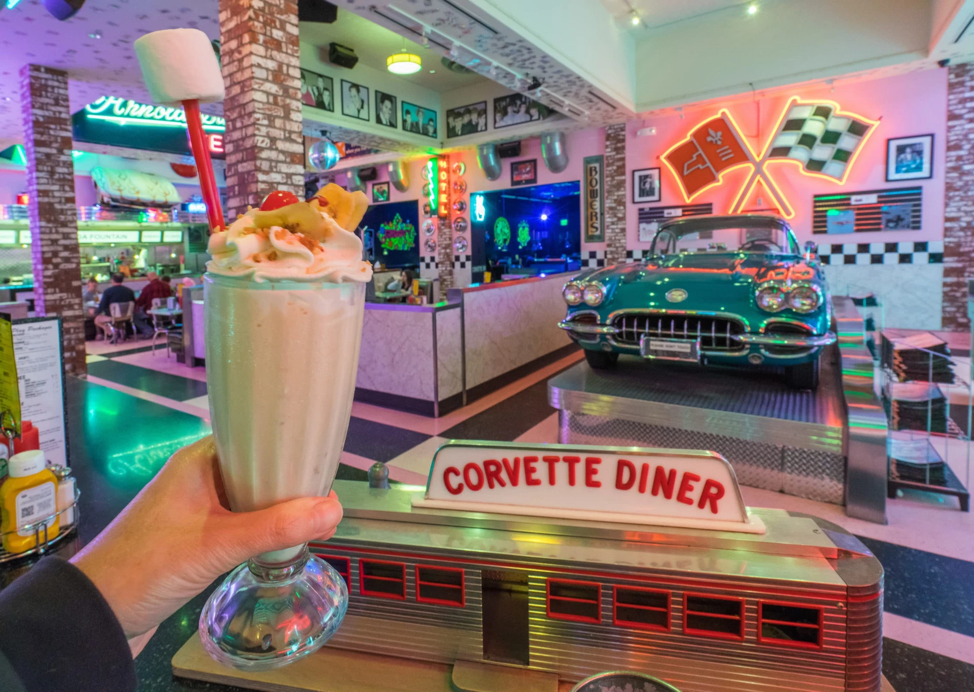 A milkshake held up in front of a vintage car at Corvette Diner in San Diego.