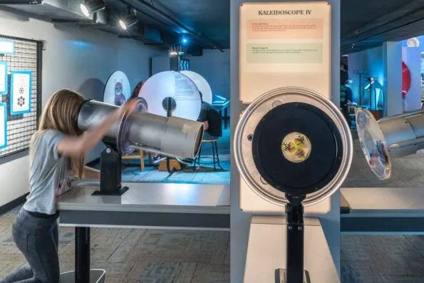 A girl looks through a larger than usual kaleidoscope at Fleet Science Center.