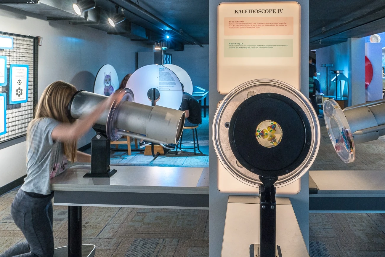 A girl looks through a larger than usual kaleidoscope at Fleet Science Center.