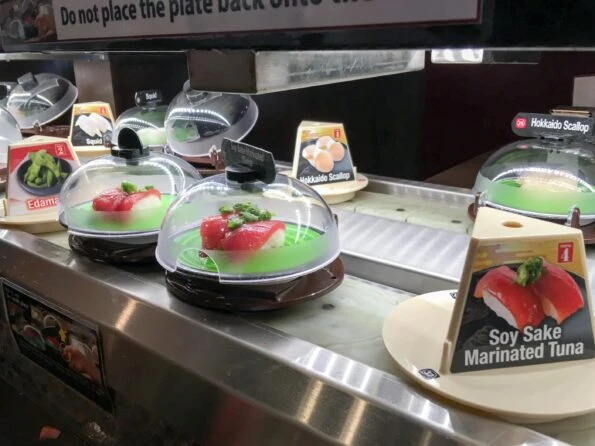 Tuna nigiri sushi under domes travels across a conveyor belt at Kura Sushi in San Diego.