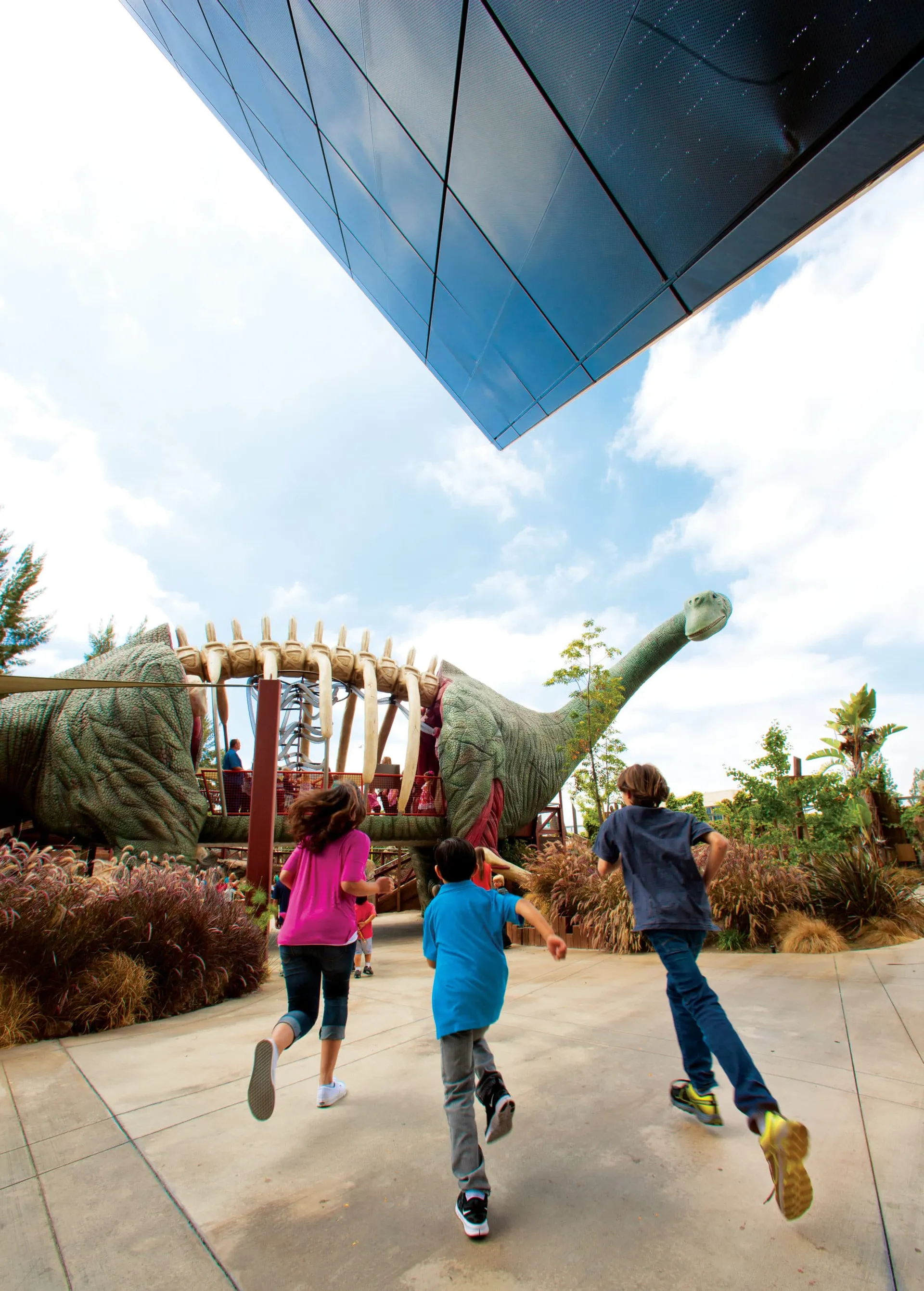 Kids run outside towards the outdoor dinosaur at The Cube in Anaheim.
