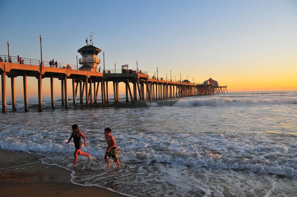 Two children run out of the ocean at sunset at Huntington Beach near the pier.