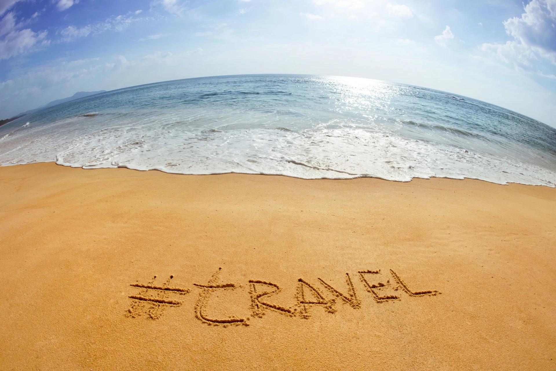The very popular Instagram hashtag, #travel, written in the sand on a beach.