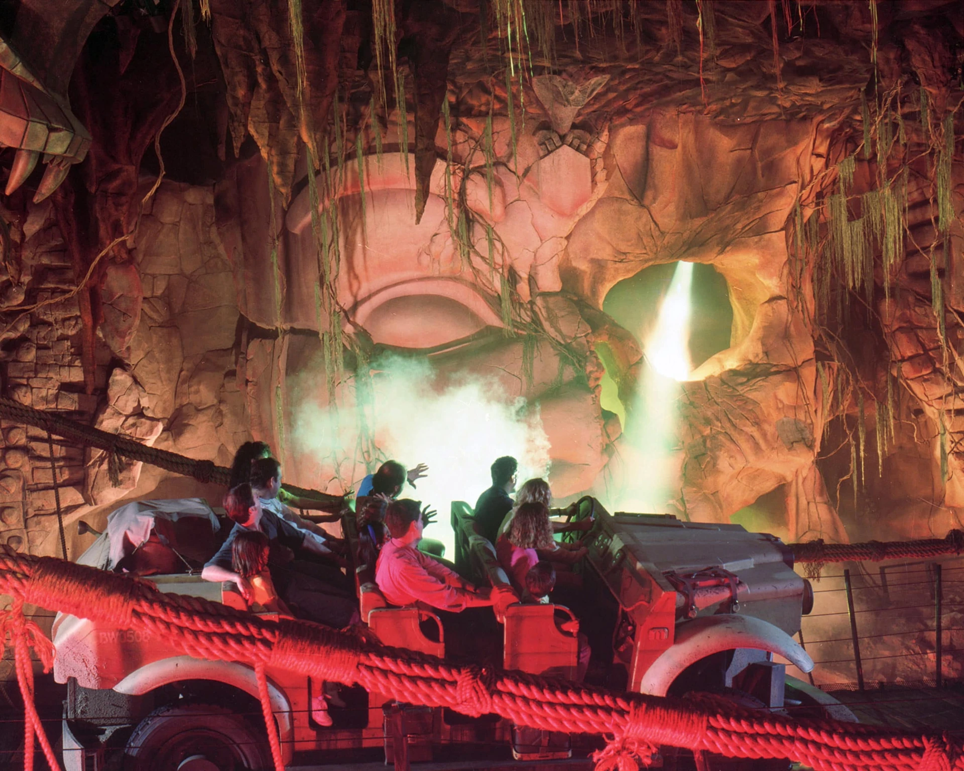 Riders in an Indiana Jones Adventure car speed past steam and flashing lights.