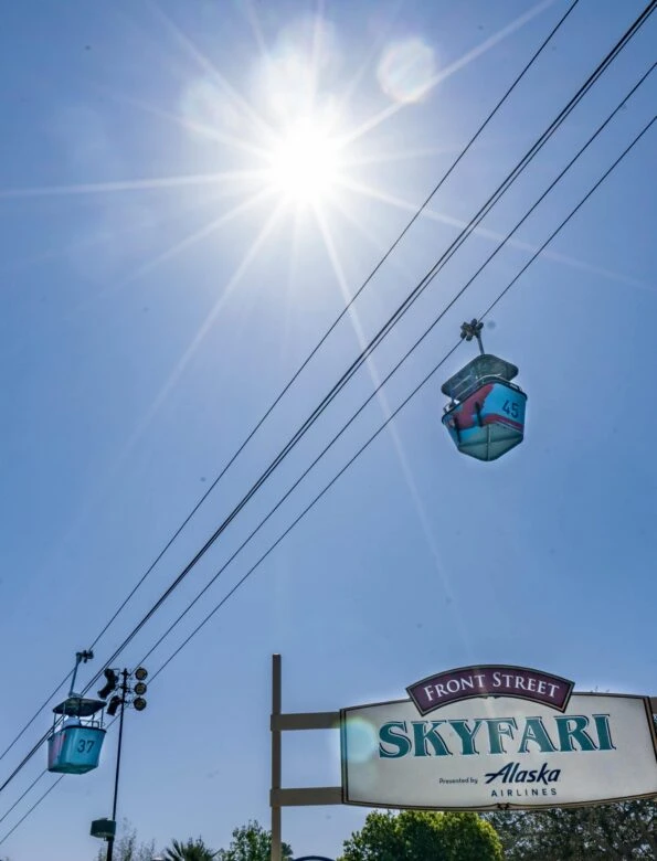 Upward view of two Skyfari aerial trams against a blue morning sky.