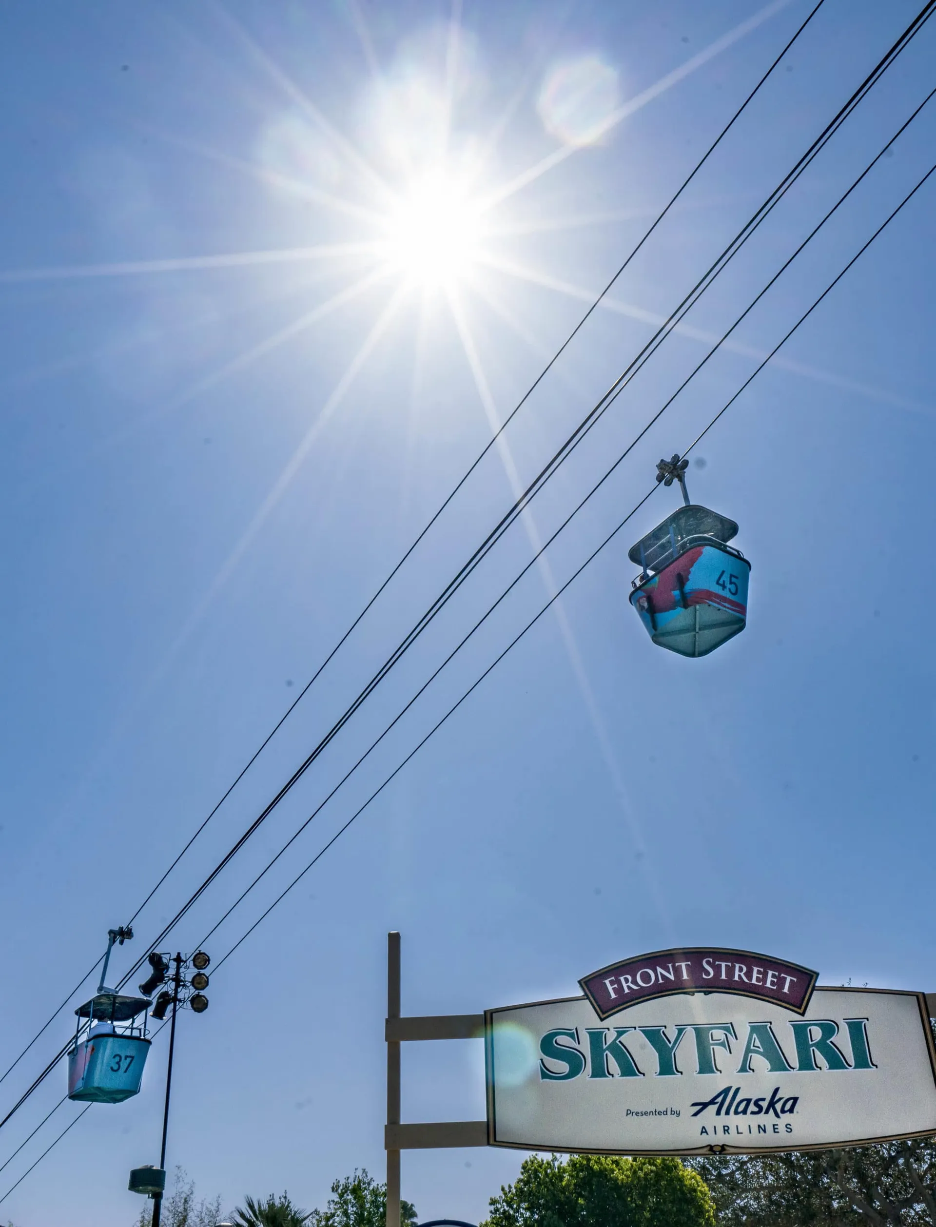 Upward view of two Skyfari aerial trams against a blue morning sky.