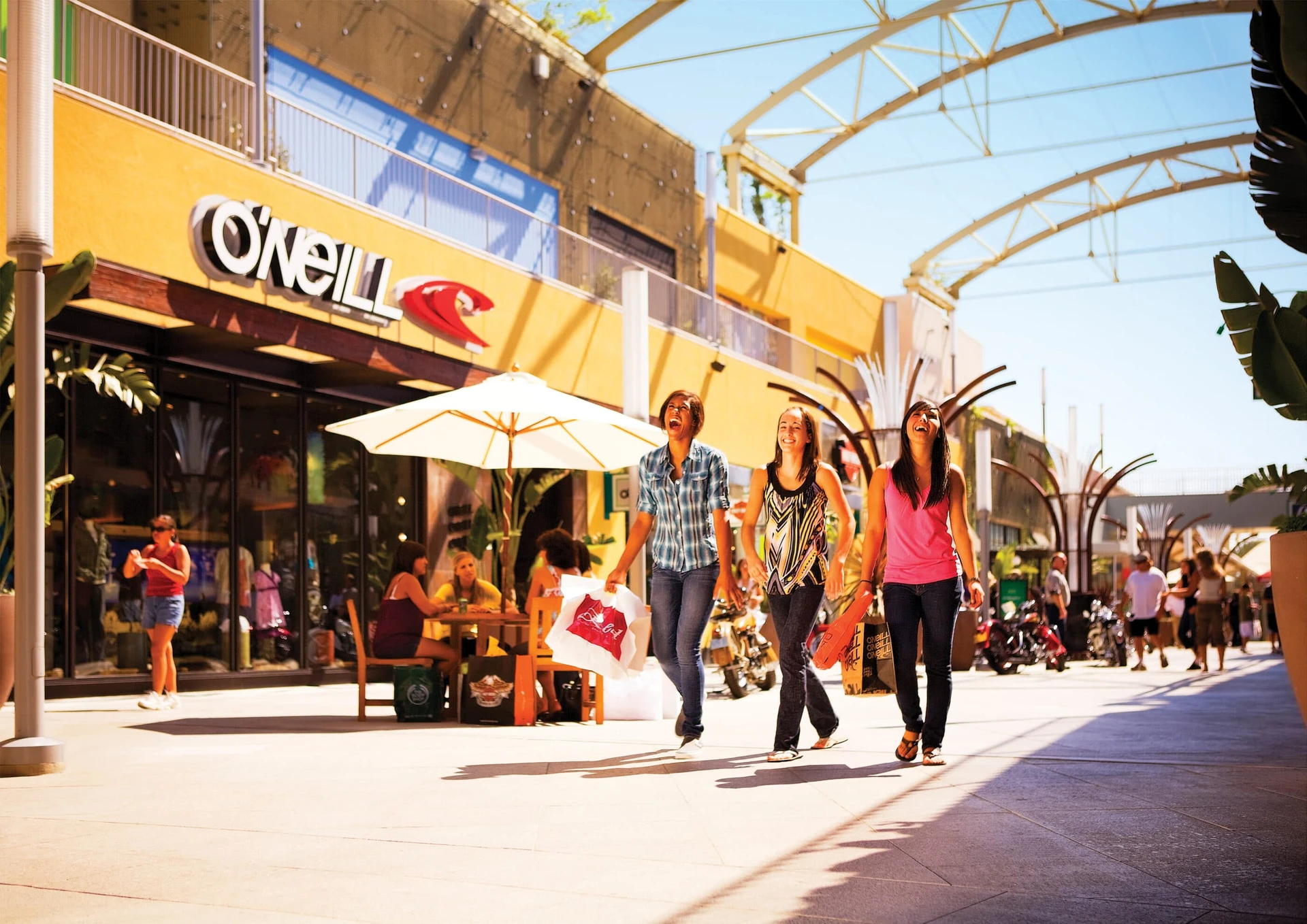 Friends walk on a sunny day past stores at Anaheim GardenWalk.
