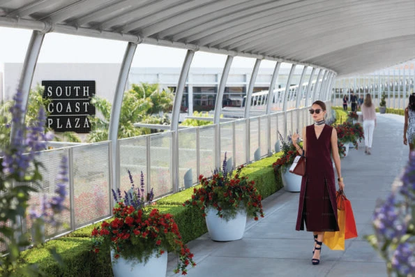 A women exits the mall down an elevated pathway carrying shopping bags at South Coast Plaza.
