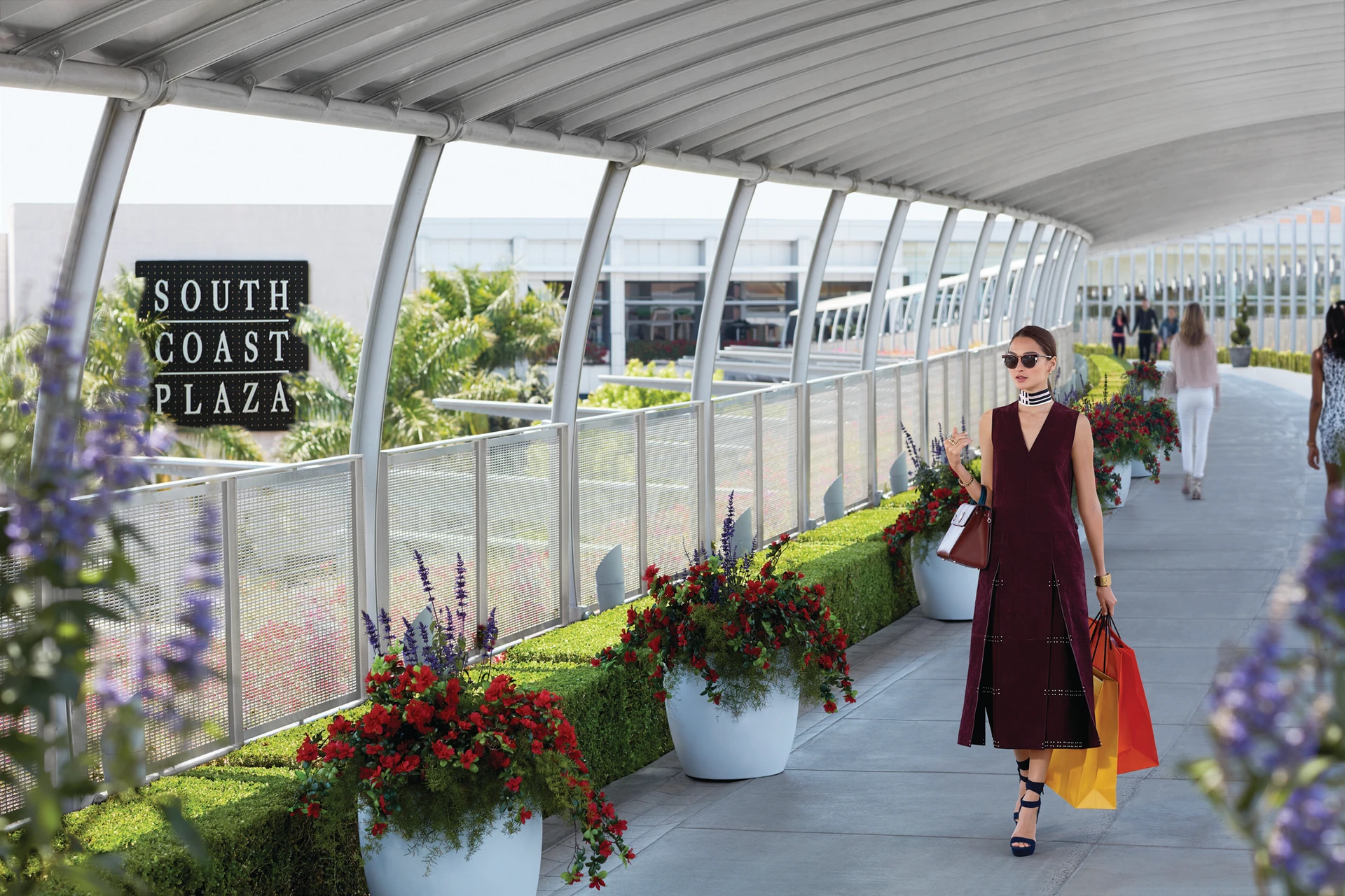 A women exits the mall down an elevated pathway carrying shopping bags at South Coast Plaza.