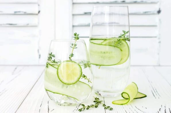 Cucumber infused hydrating water with thyme and lime on rustic old wooden table.