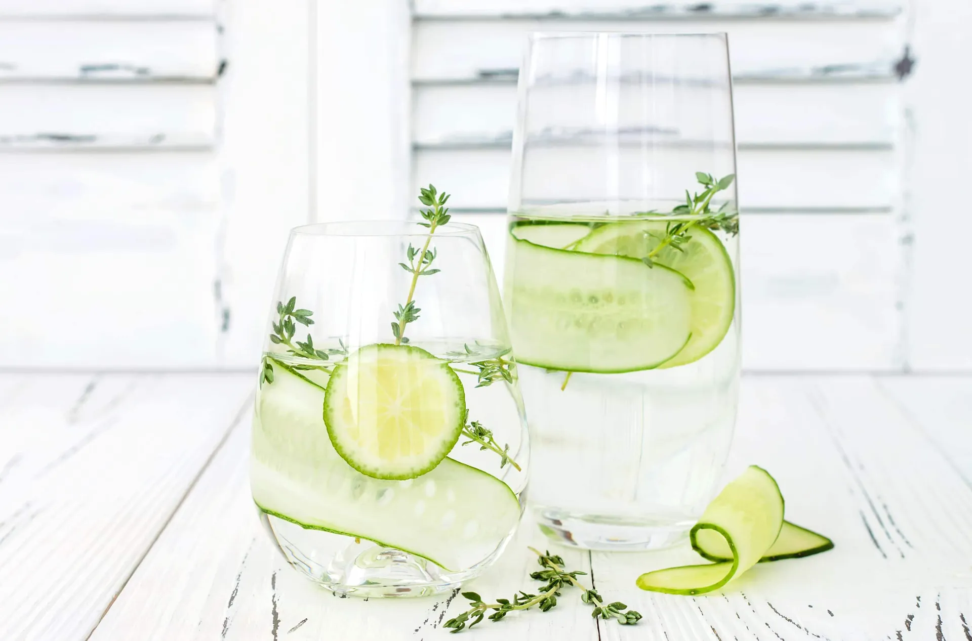 Cucumber infused hydrating water with thyme and lime on rustic old wooden table.