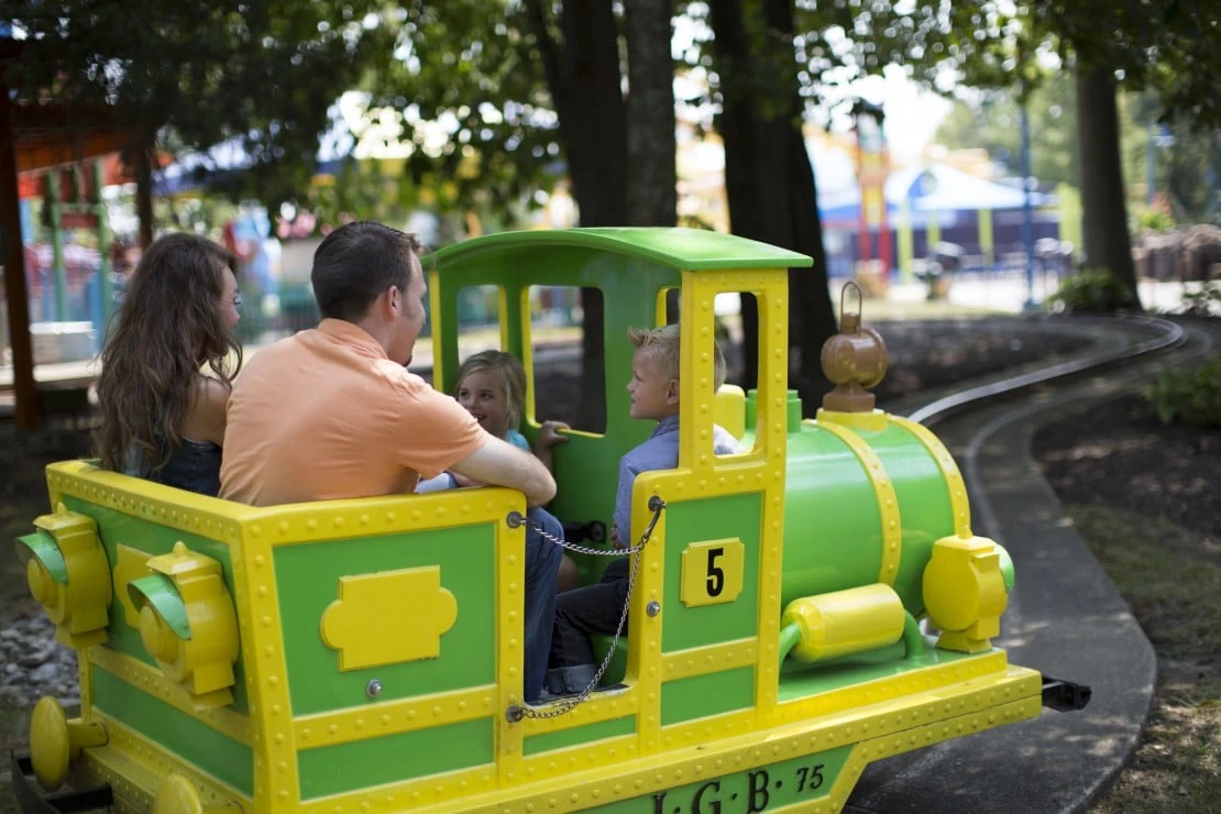 A family with young kids rides on a small train at Kings Island theme park.