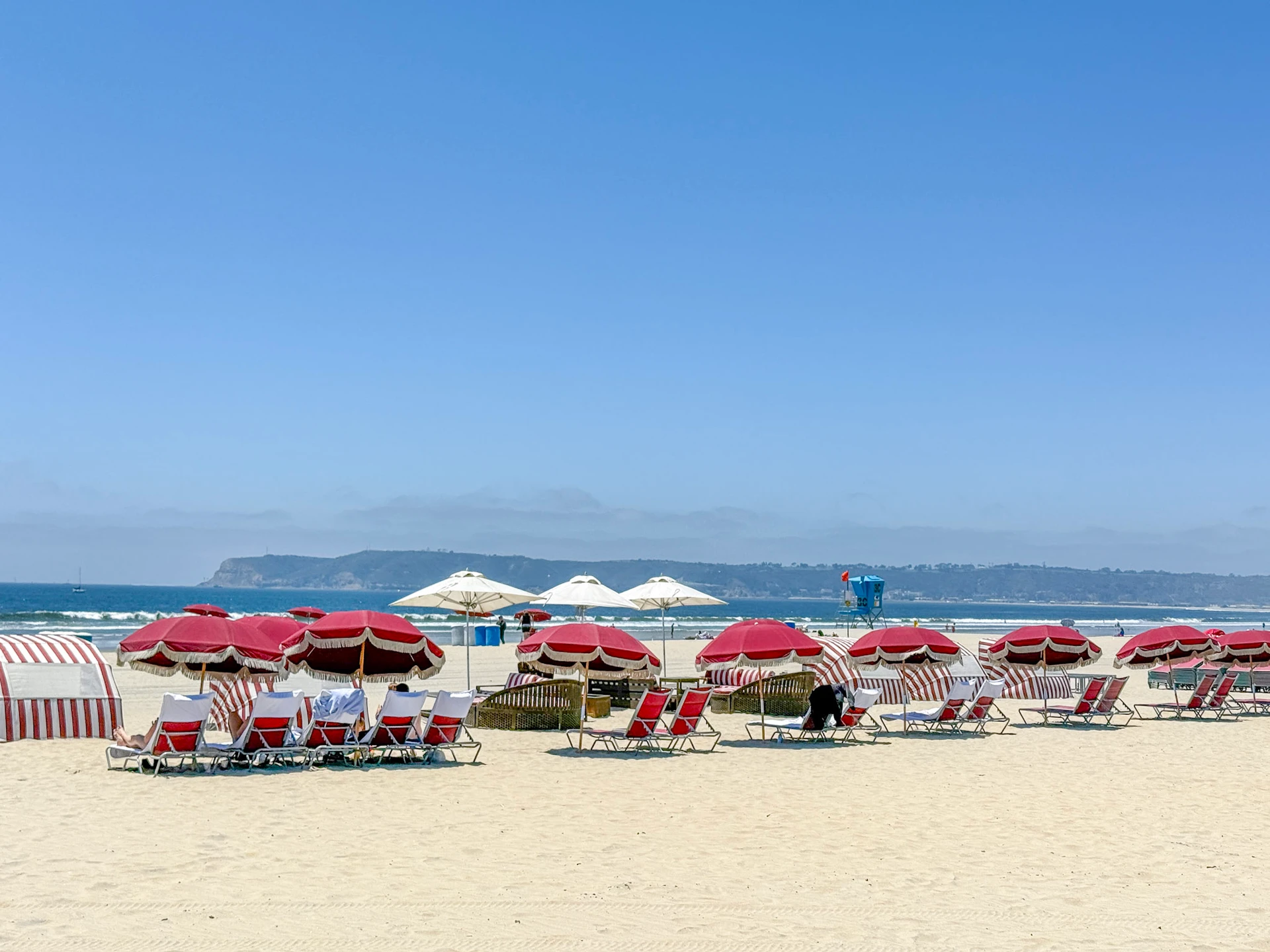Red chairs and umbrellas ready on the sand at Del Beach.