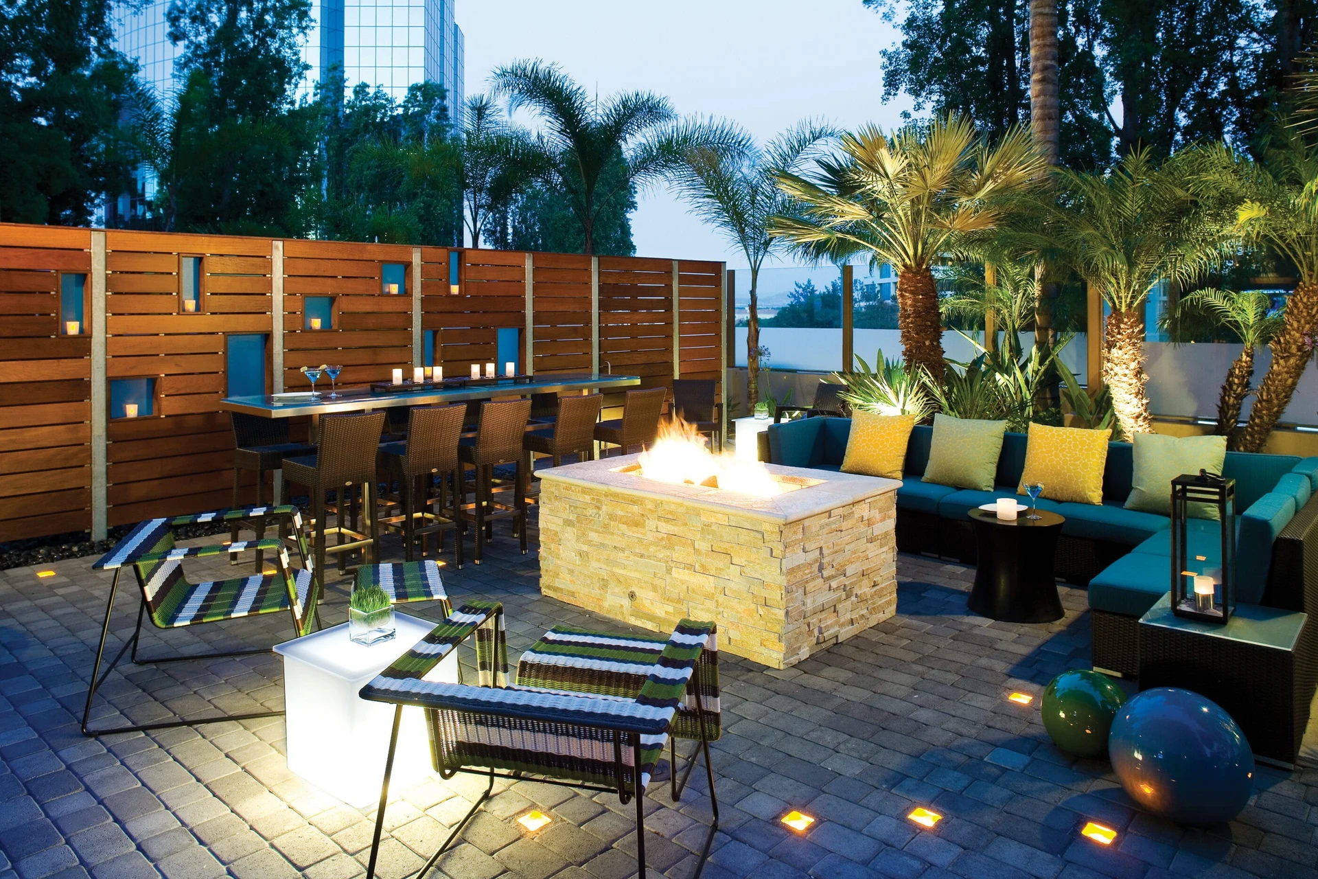 The outdoor lounge area surrounds a lit fire pit at dusk at Embassy Suites La Jolla.