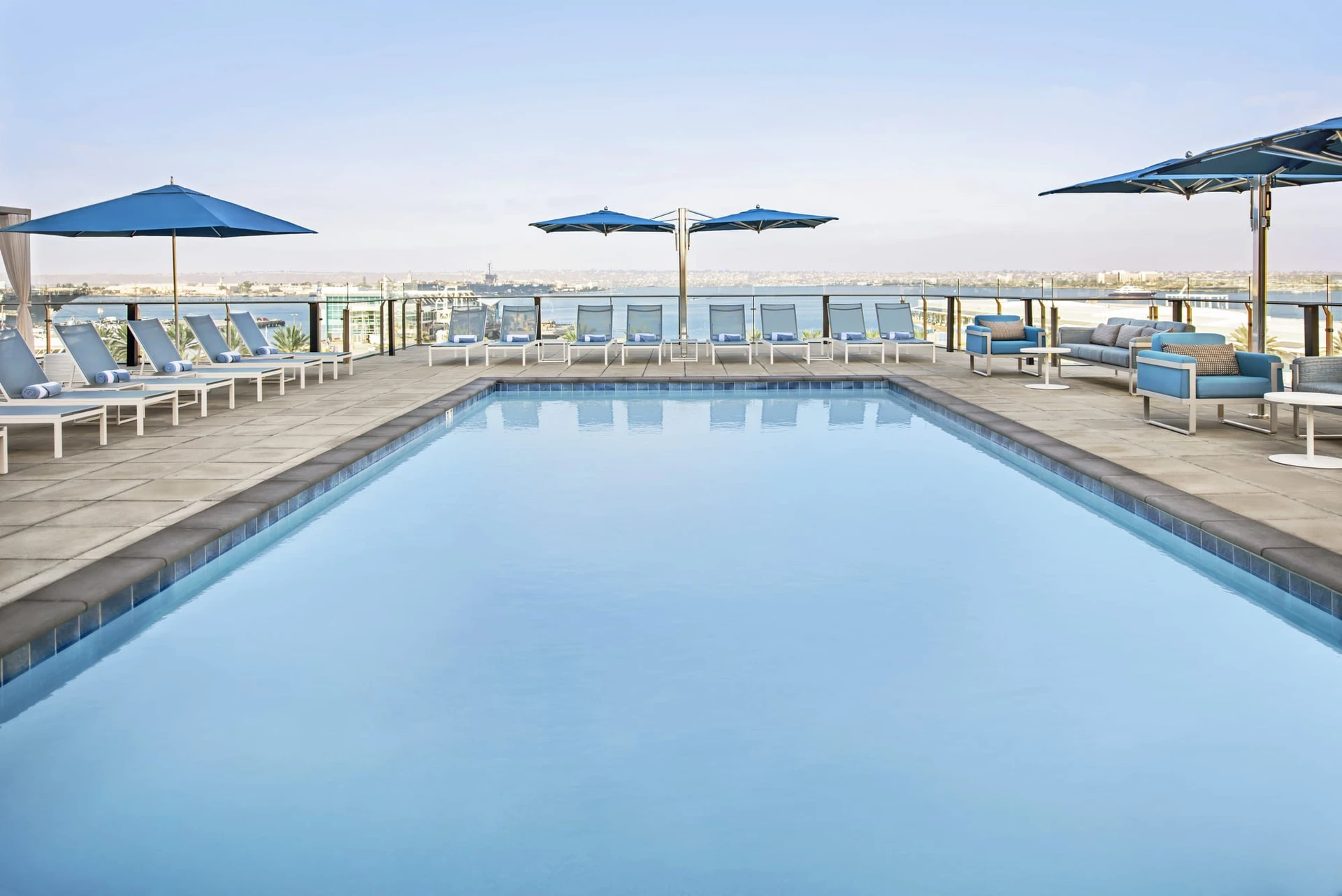 Open-air pool deck surrounded by lounge chairs, overlooking San Diego Bay.