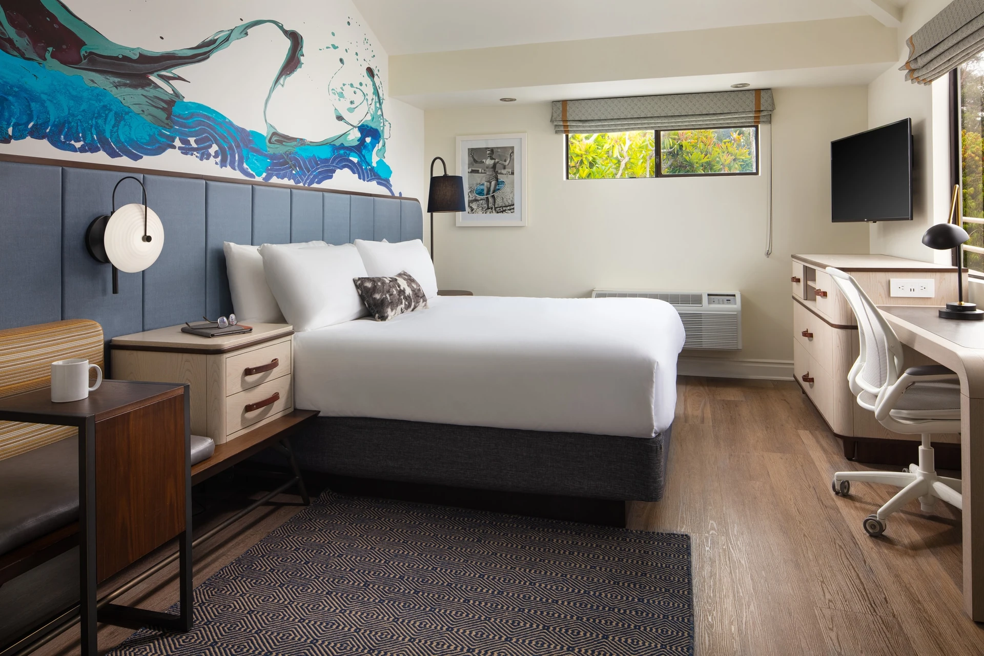 A king bed room with a beach theme of grey and neutral colors with blue wave art on the wall.