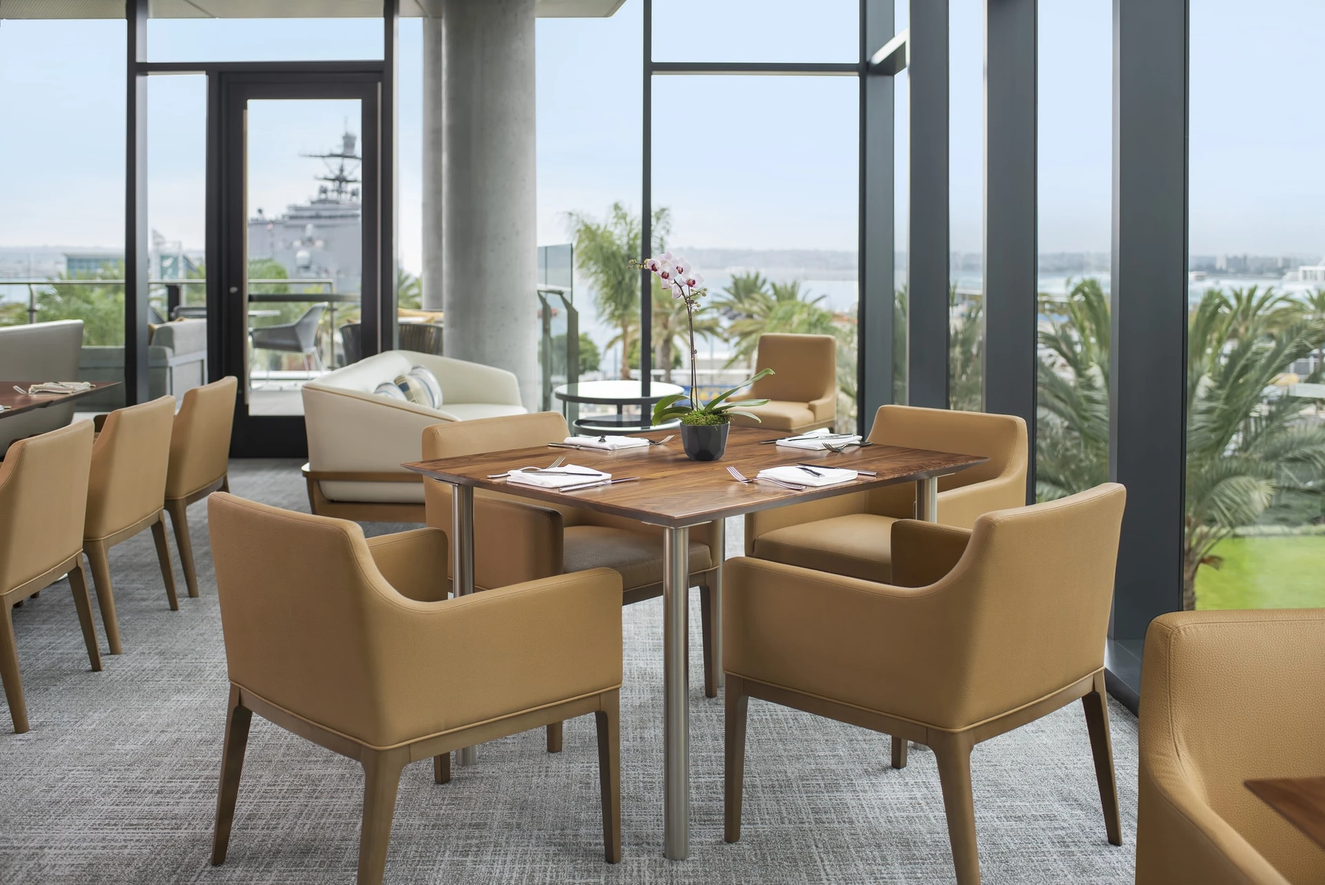 Tables in the Club Lounge set against tall glass walls with views overlooking the bay.