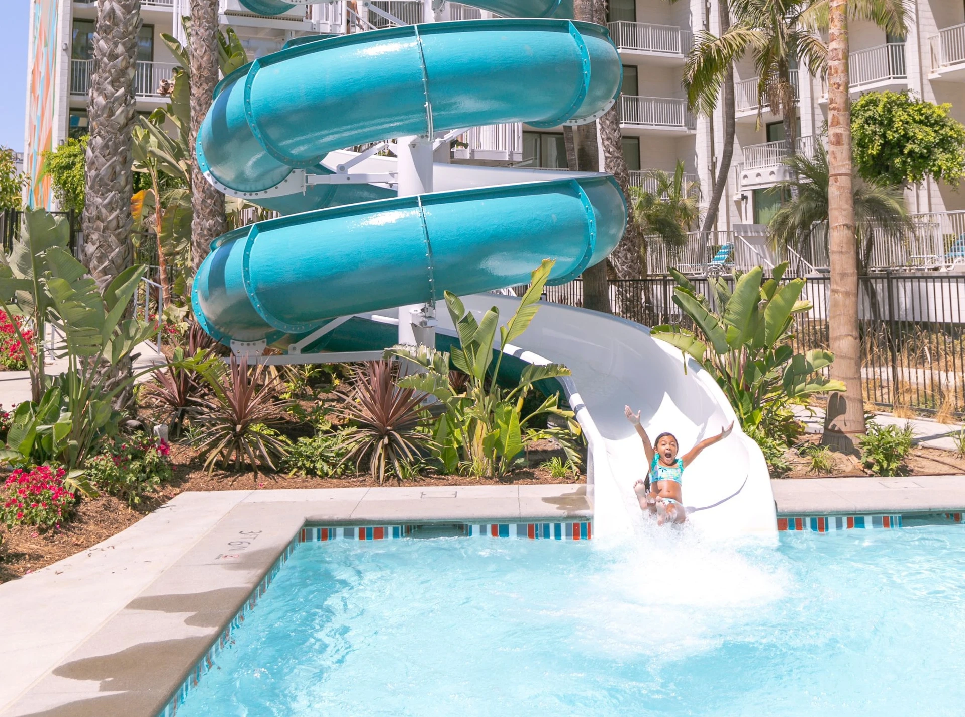 A little girl rides down the water slide into the swimming pool.