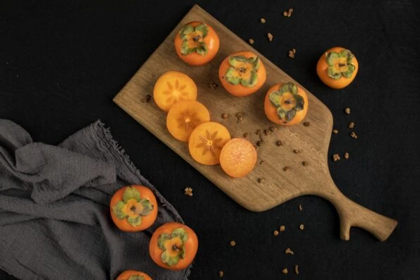 Whole and sliced persimmon fruit on a cutting board against a black table cloth.