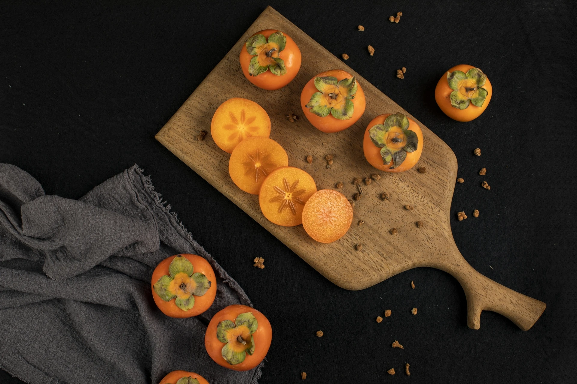 Whole and sliced persimmon fruit on a cutting board against a black table cloth.