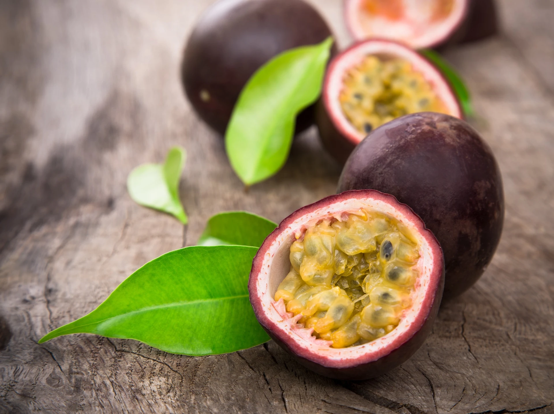 Passion fruits, cut open and whole, on wooden background.