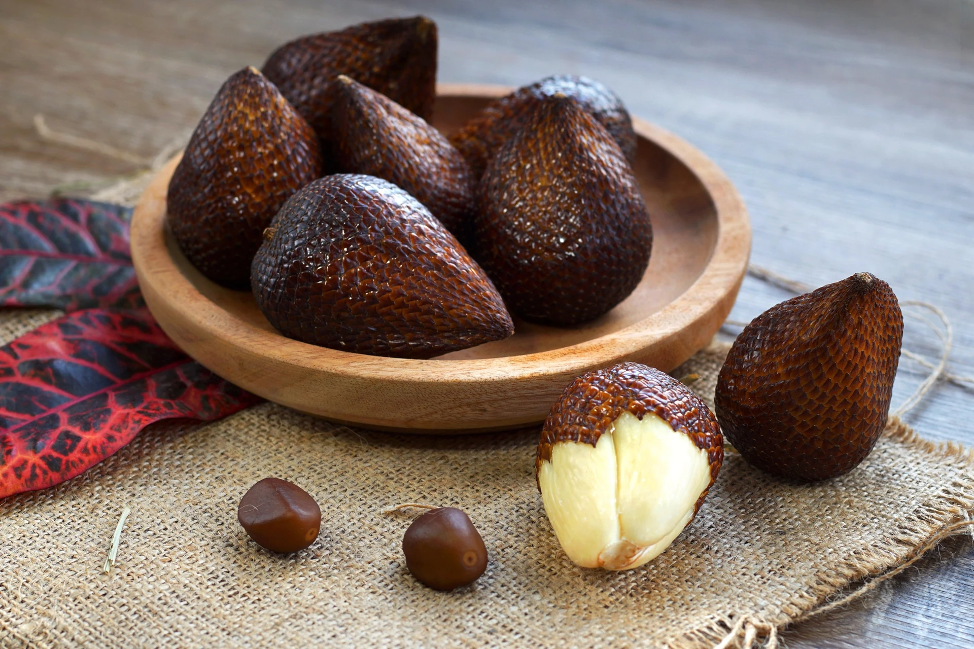 Whole snake fruit in a bowl on a burlap place mat next to a peeled snake fruit.