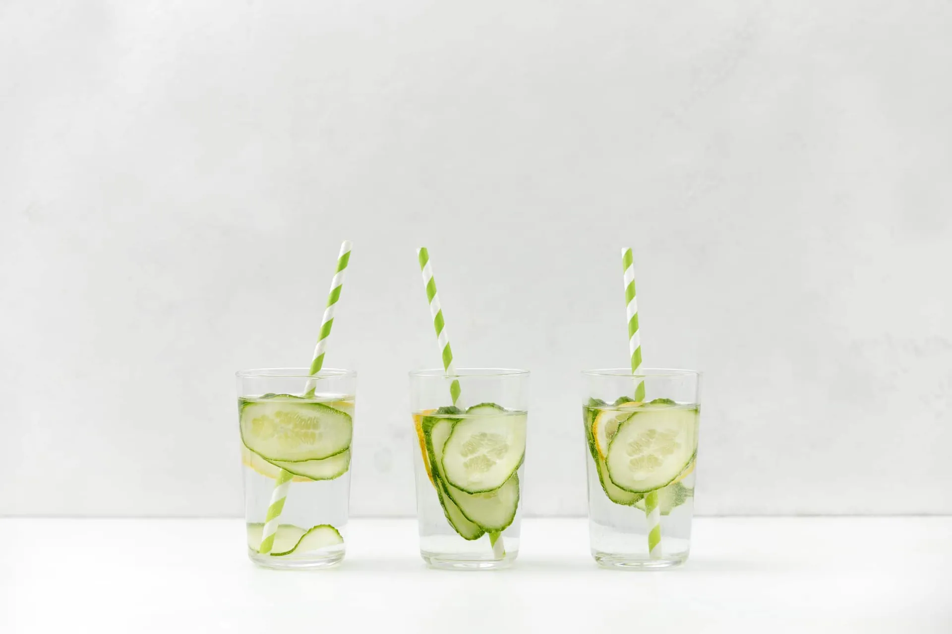 Cucumber infused ready to drink clear water served in transparent glasses with straws, front view