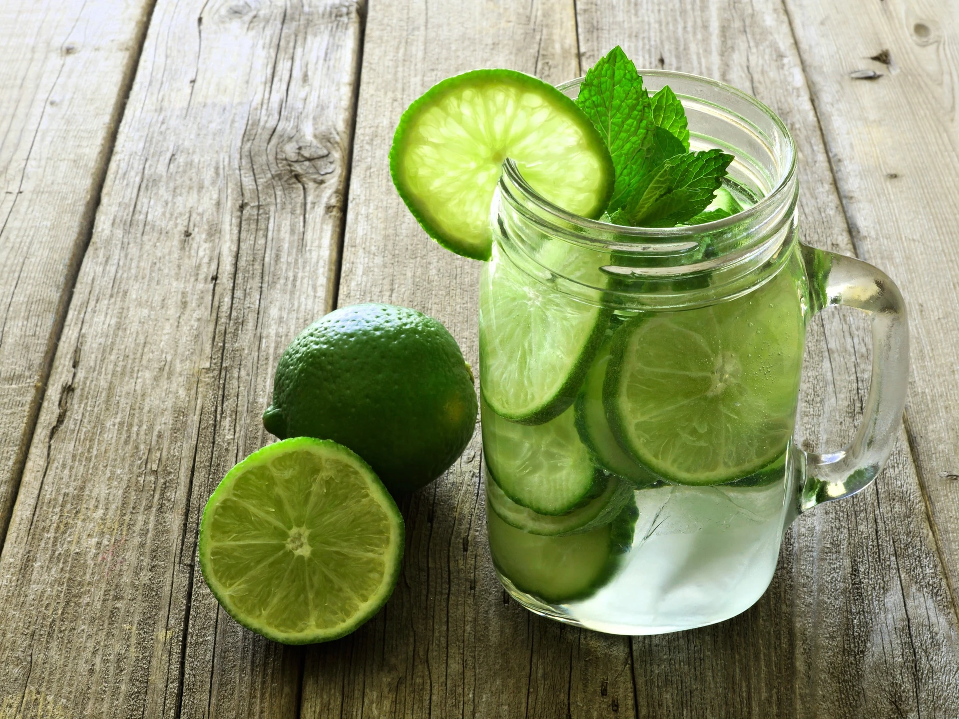 Detox water with lime and cucumbers in a mason jar against a rustic wood background
