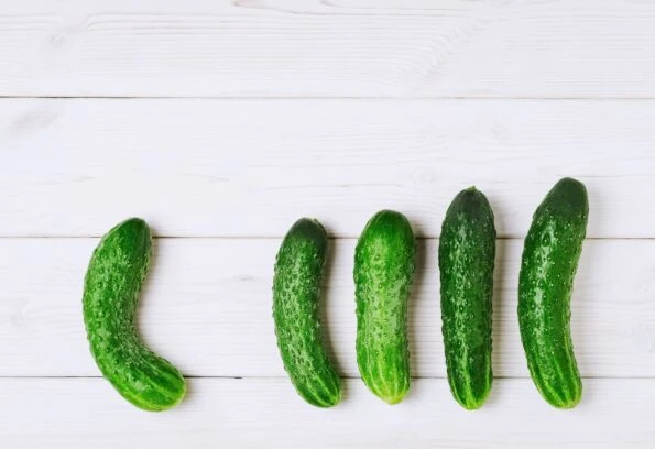 Five whole cucumbers lined up on a table.