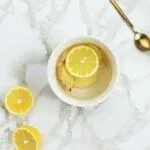 A cup of warm lemon water with ginger on a marble table.
