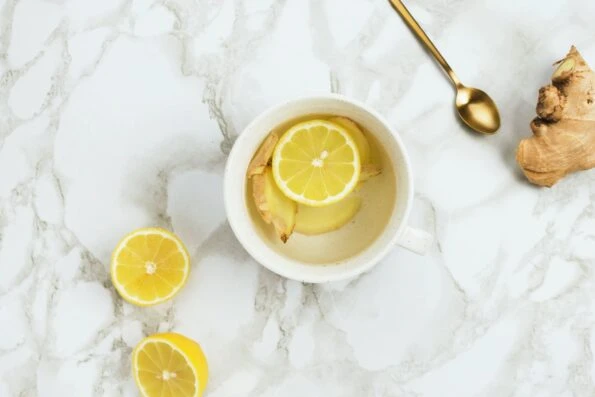 A cup of warm lemon water with ginger on a marble table.