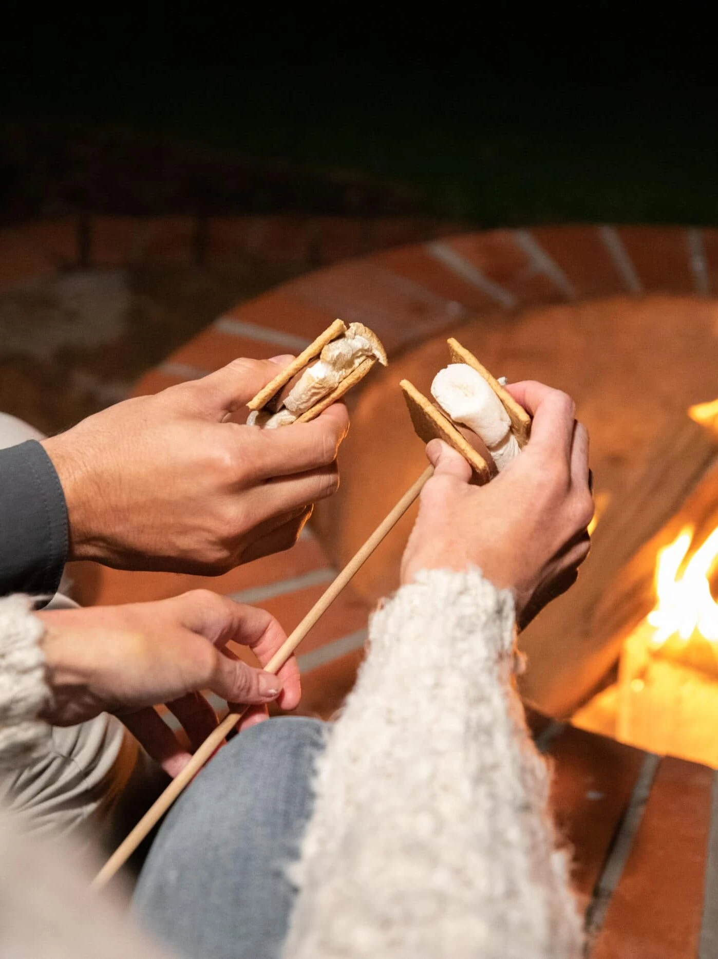 Two people roast s'mores over a hotel fire pit.