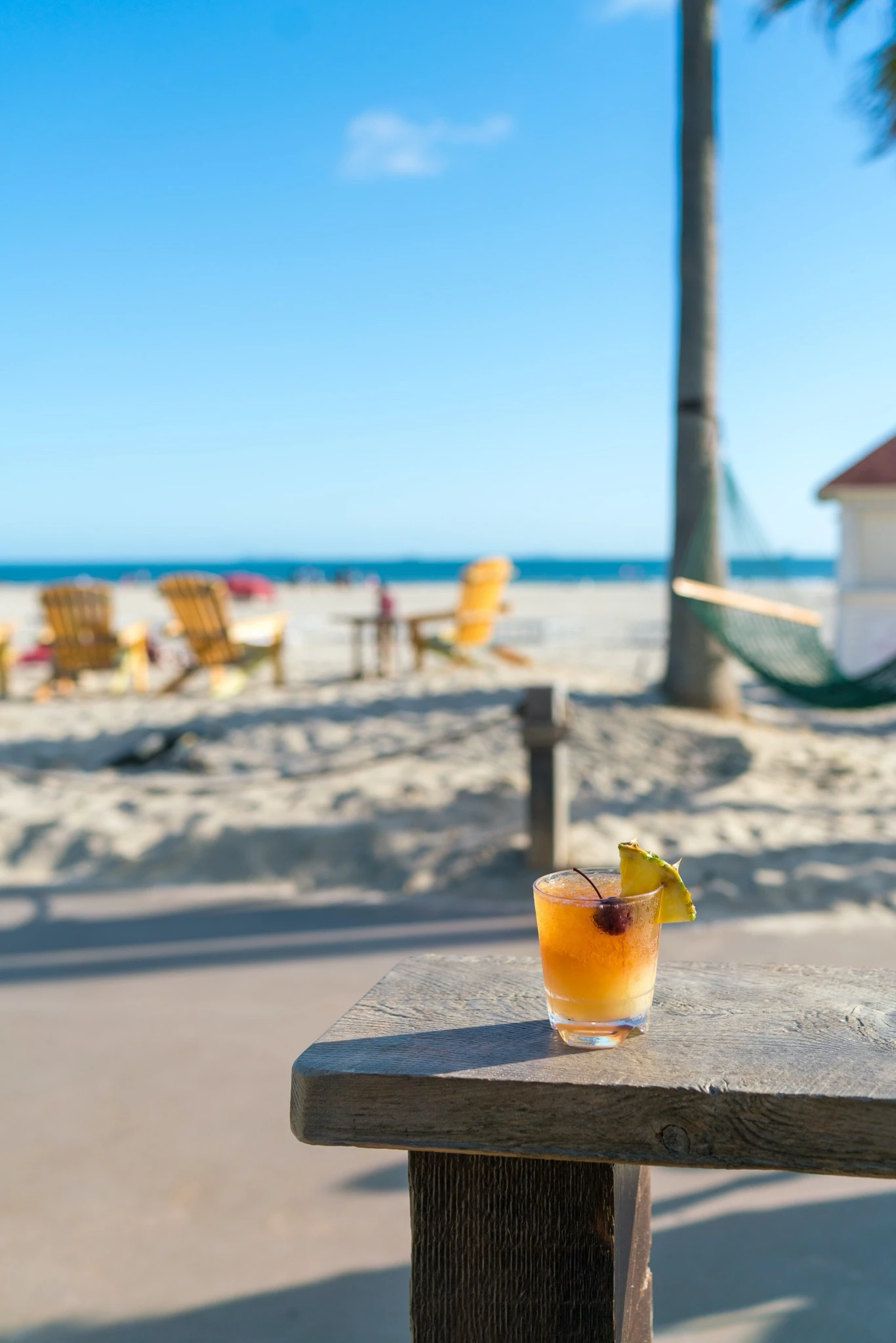 A Mai Tai cocktail sits on a ledge with the ocean and beach behind it.