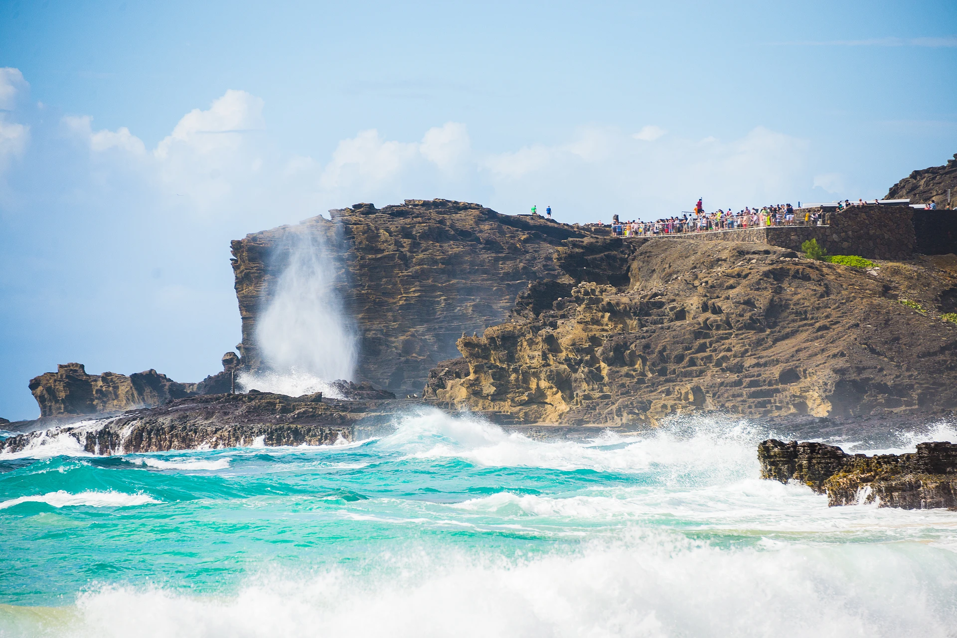 People stand on the cliffs near the blowhole as it spouts.