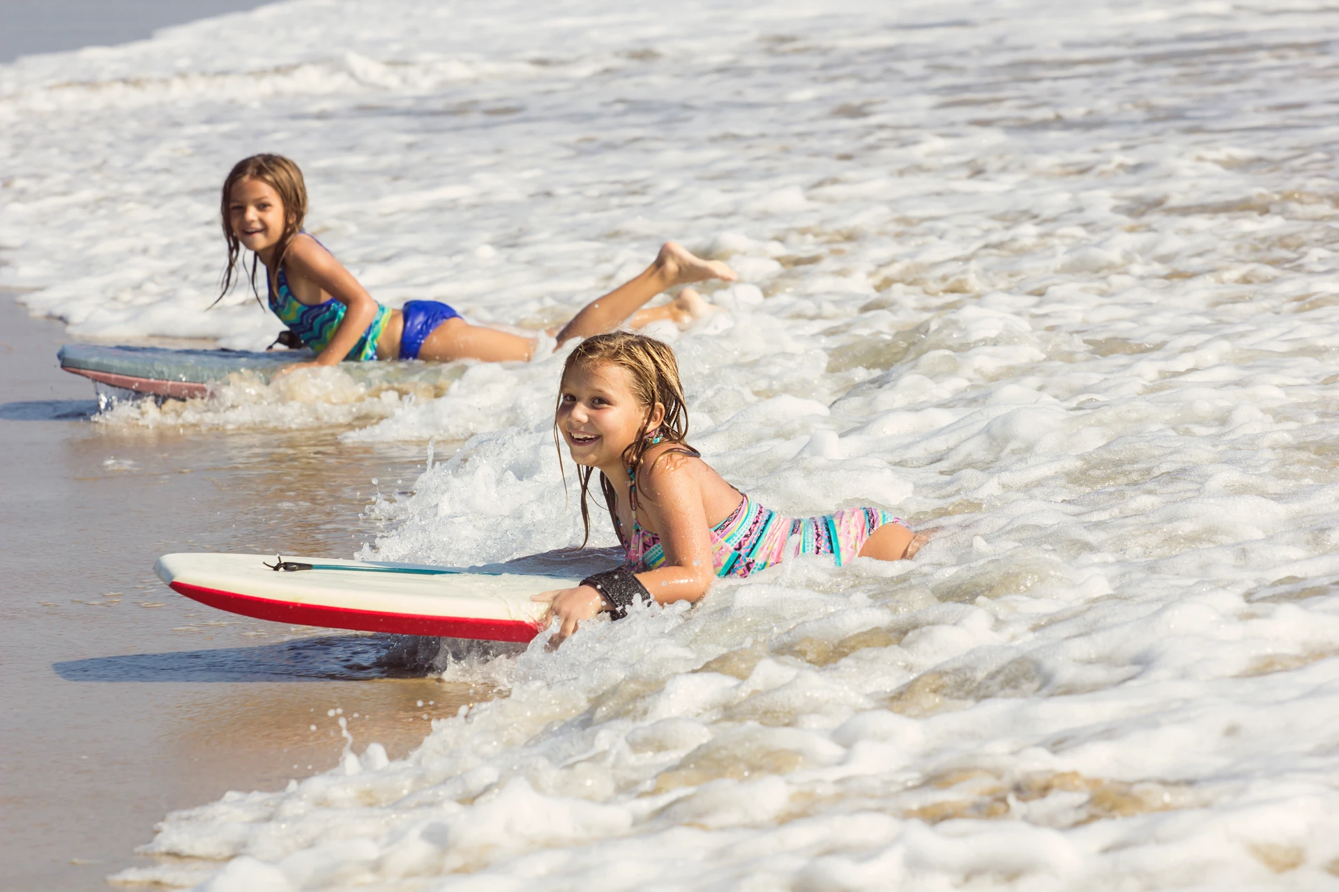 Two girls ride boogie boards into shore on a California beach.