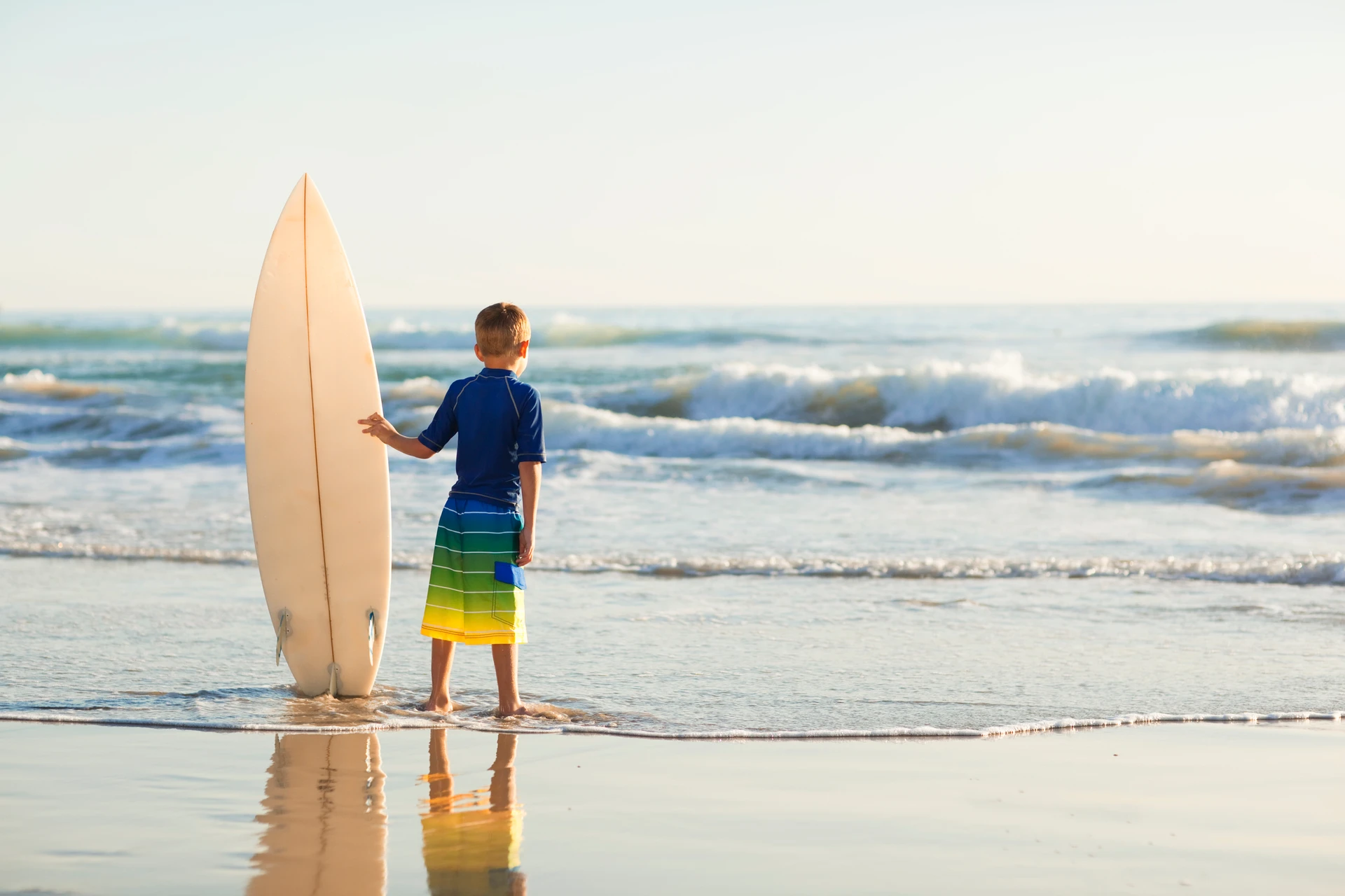 A little boy holds a surfboard on a California beach.