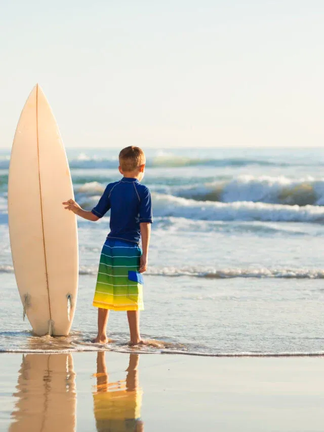 A little boy holds a surfboard on a California beach.