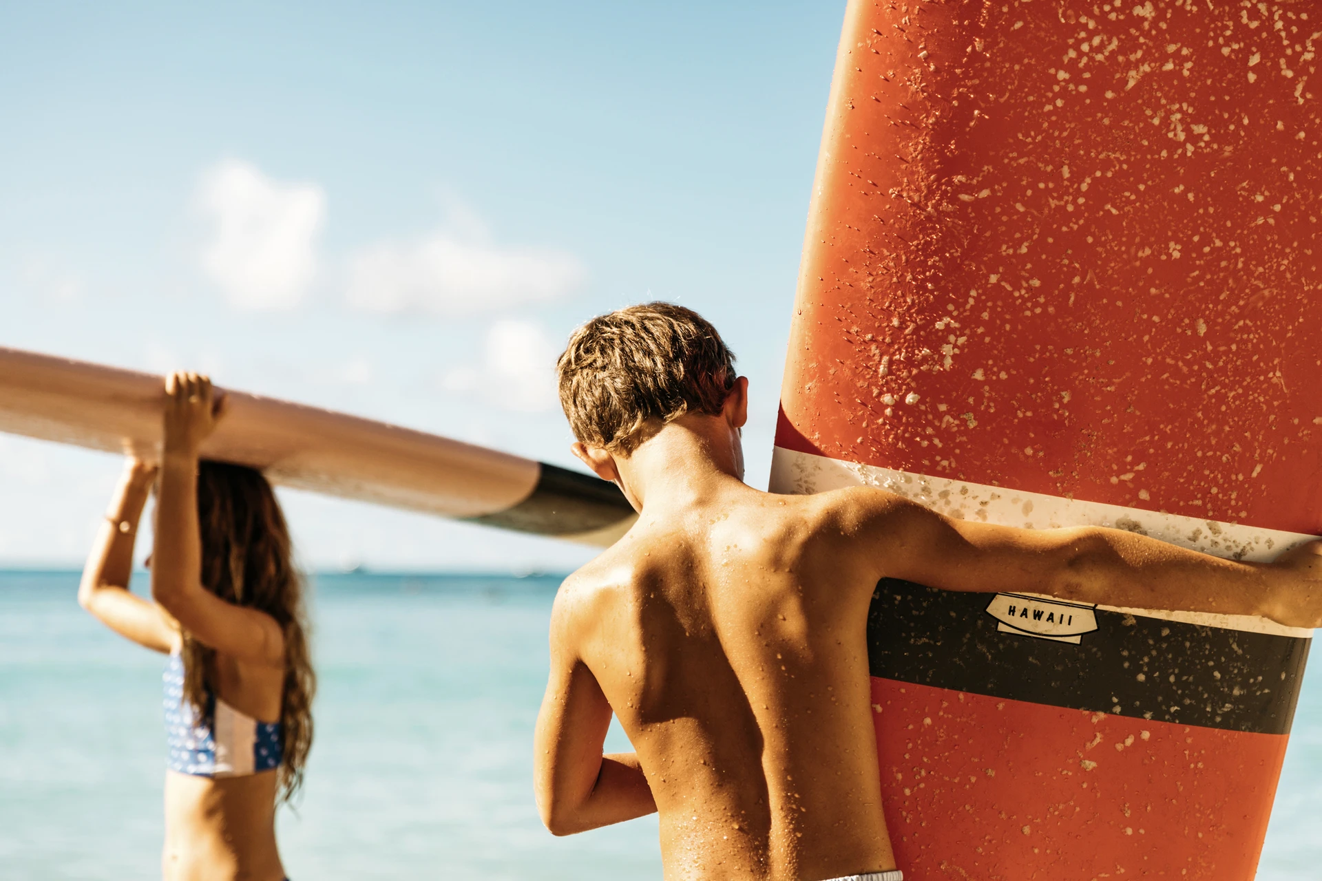 Two kids carry surfboards on a beach in Maui.
