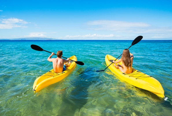 A couple each paddle yellow kayaks out into clear Maui water.