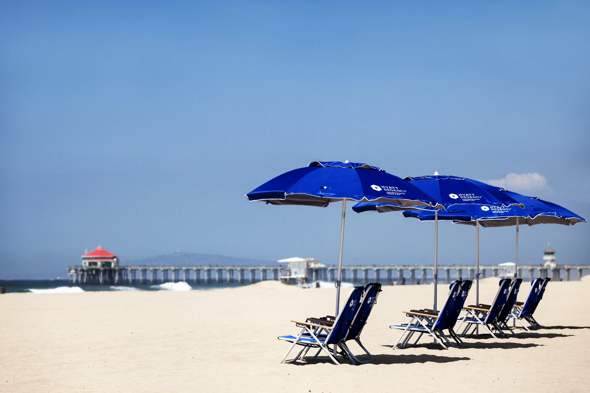 Hotel chairs and umbrellas set in the sand in front of Hyatt Regency Huntington Beach.