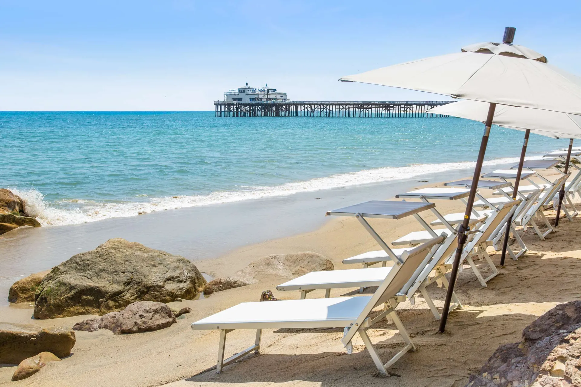 White beach lounge chairs and umbrella set up on the beach in front of Malibu Beach Inn.