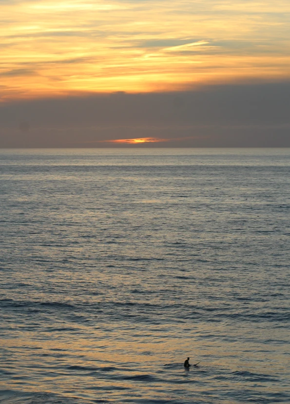 A surfer waiting for waves at sunset at D Street Beach in Encinitas.