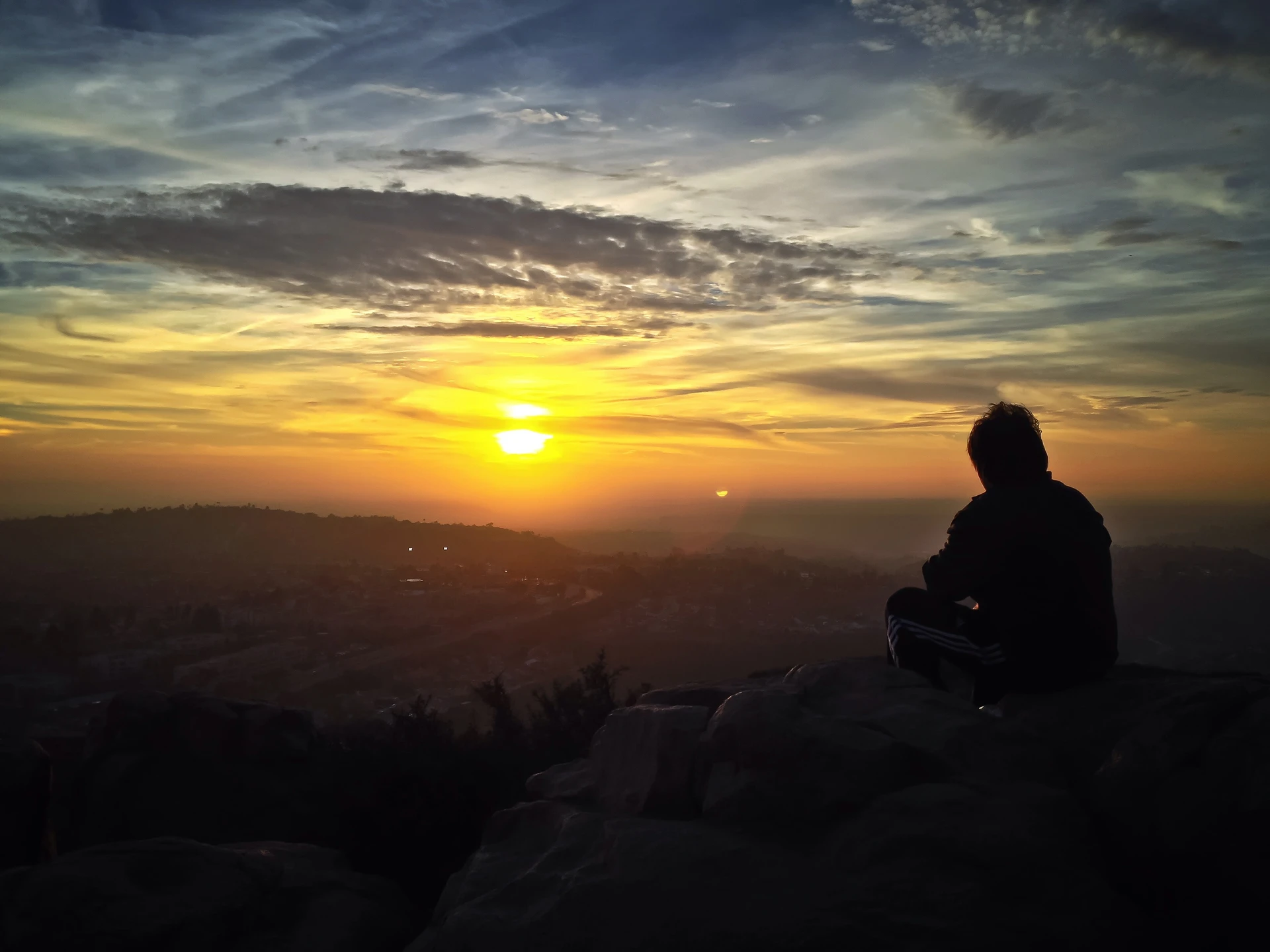 A person sits on a hillside to watch the sunset at Cowles Mountain San Diego.