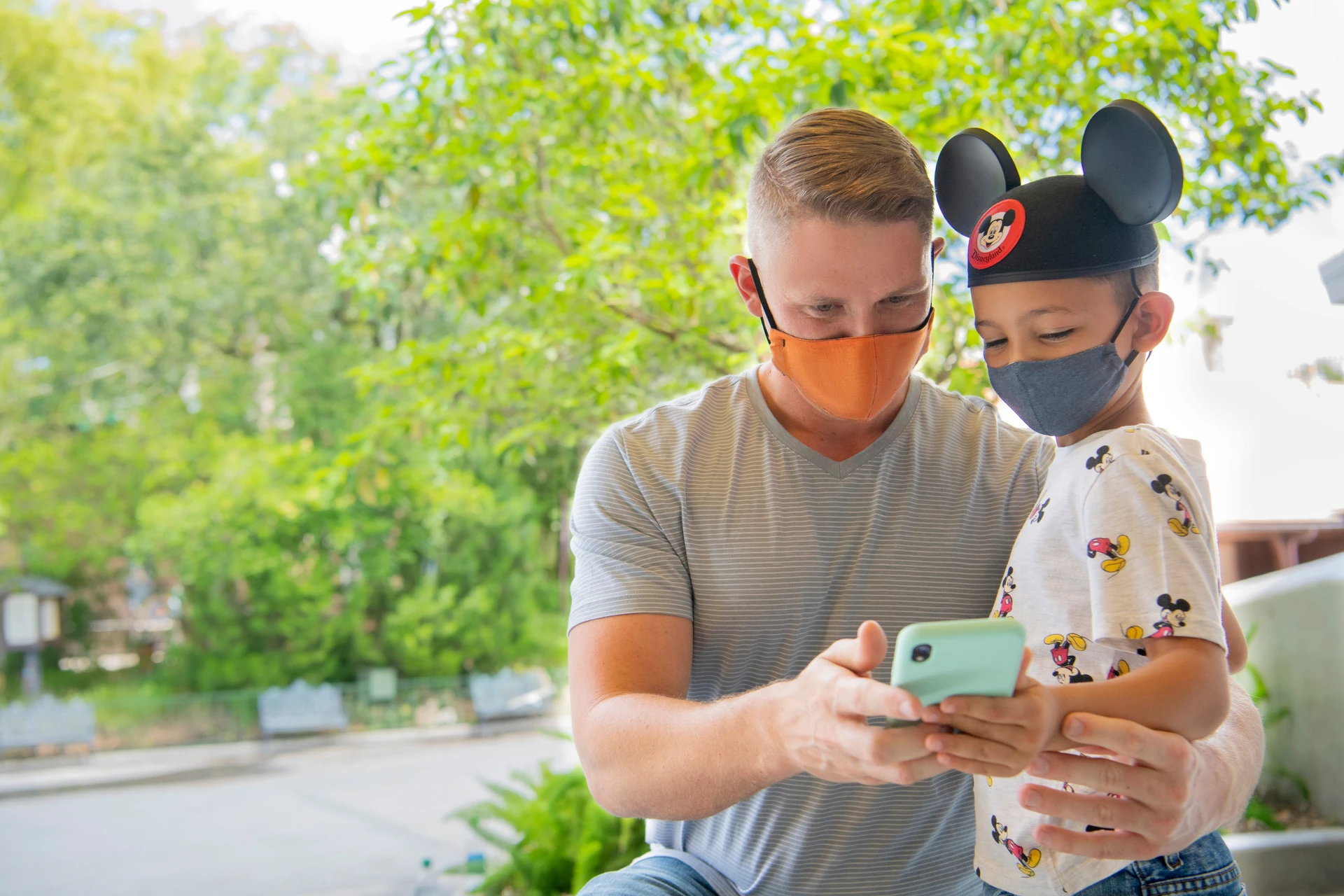 A father and son wearing Mickey ears use the Disneyland app on a cell phone.