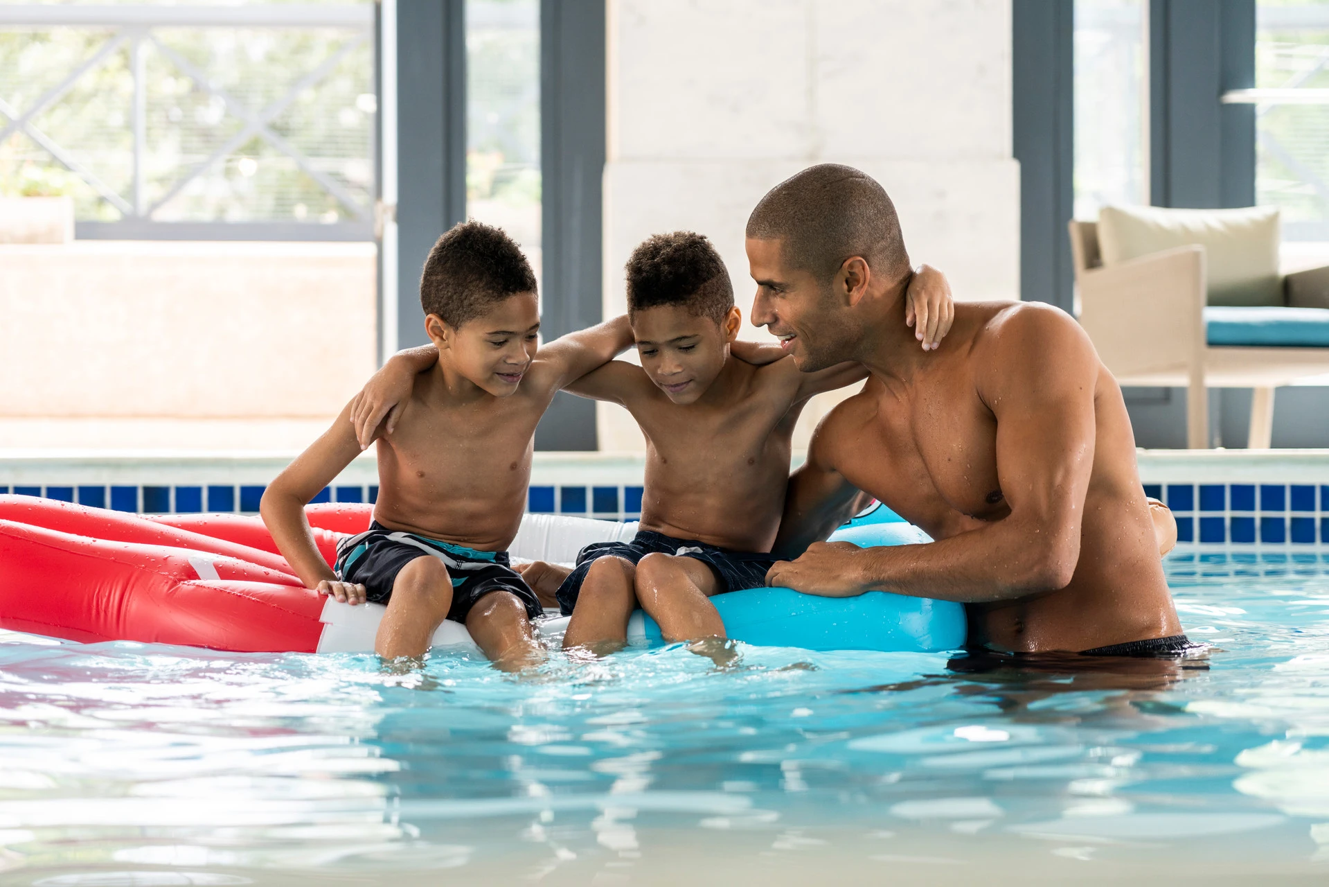 A father and two boys play in the pool.