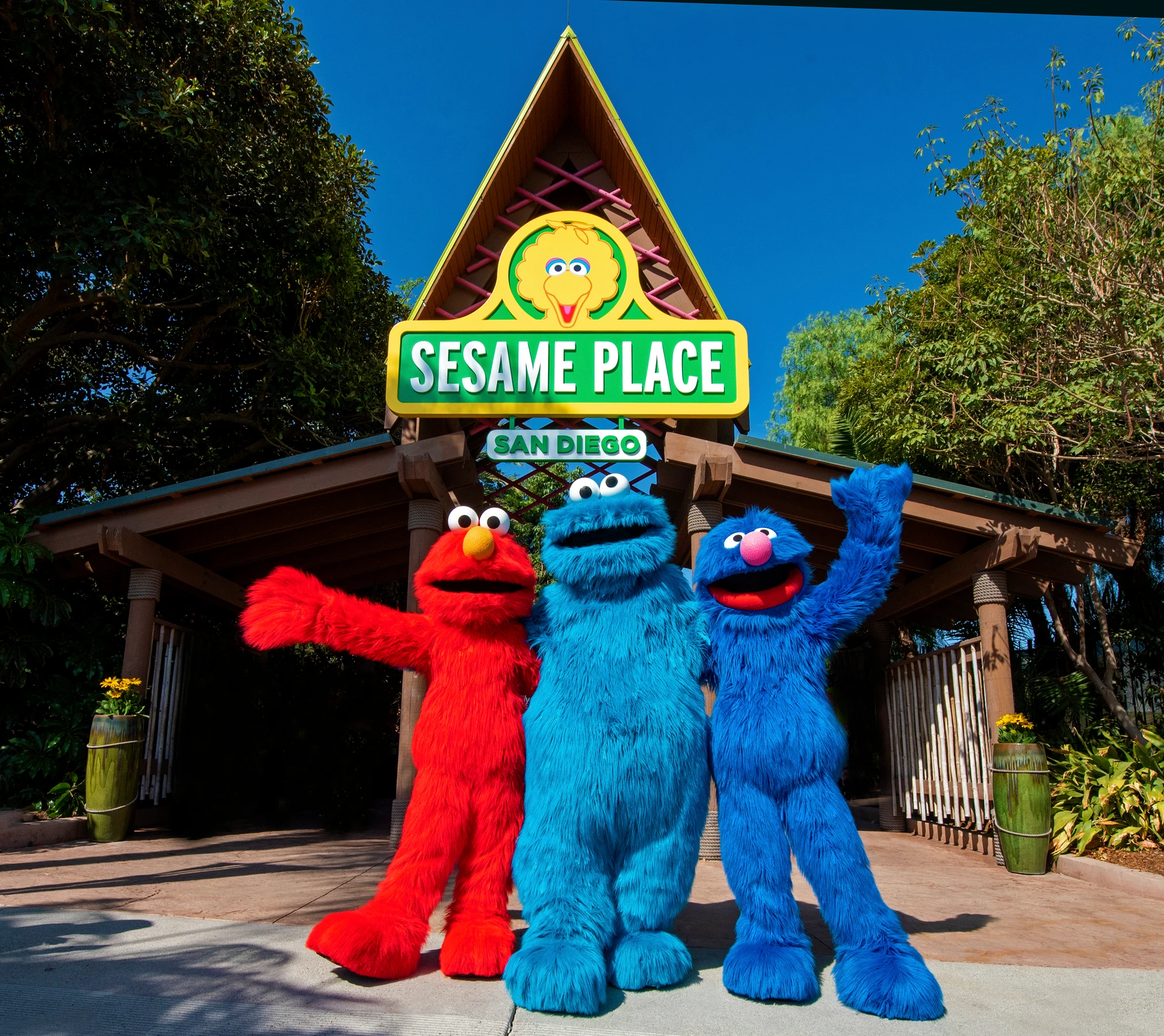 Elmo, Grover, and Cookie Monster stand in front of the entrance to Sesame Place San Diego.