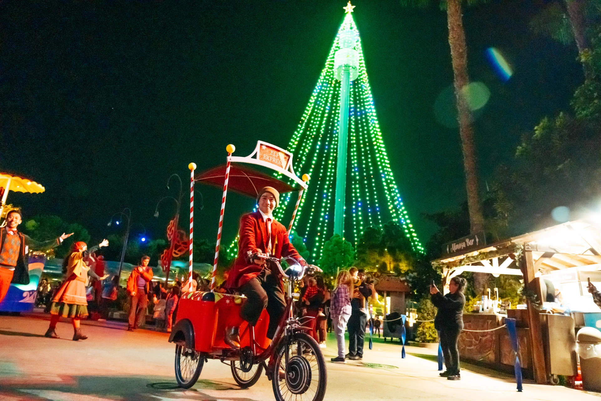 A man rides an Elf Express bike in front of the SeaWorld San Diego Christmas Tree.