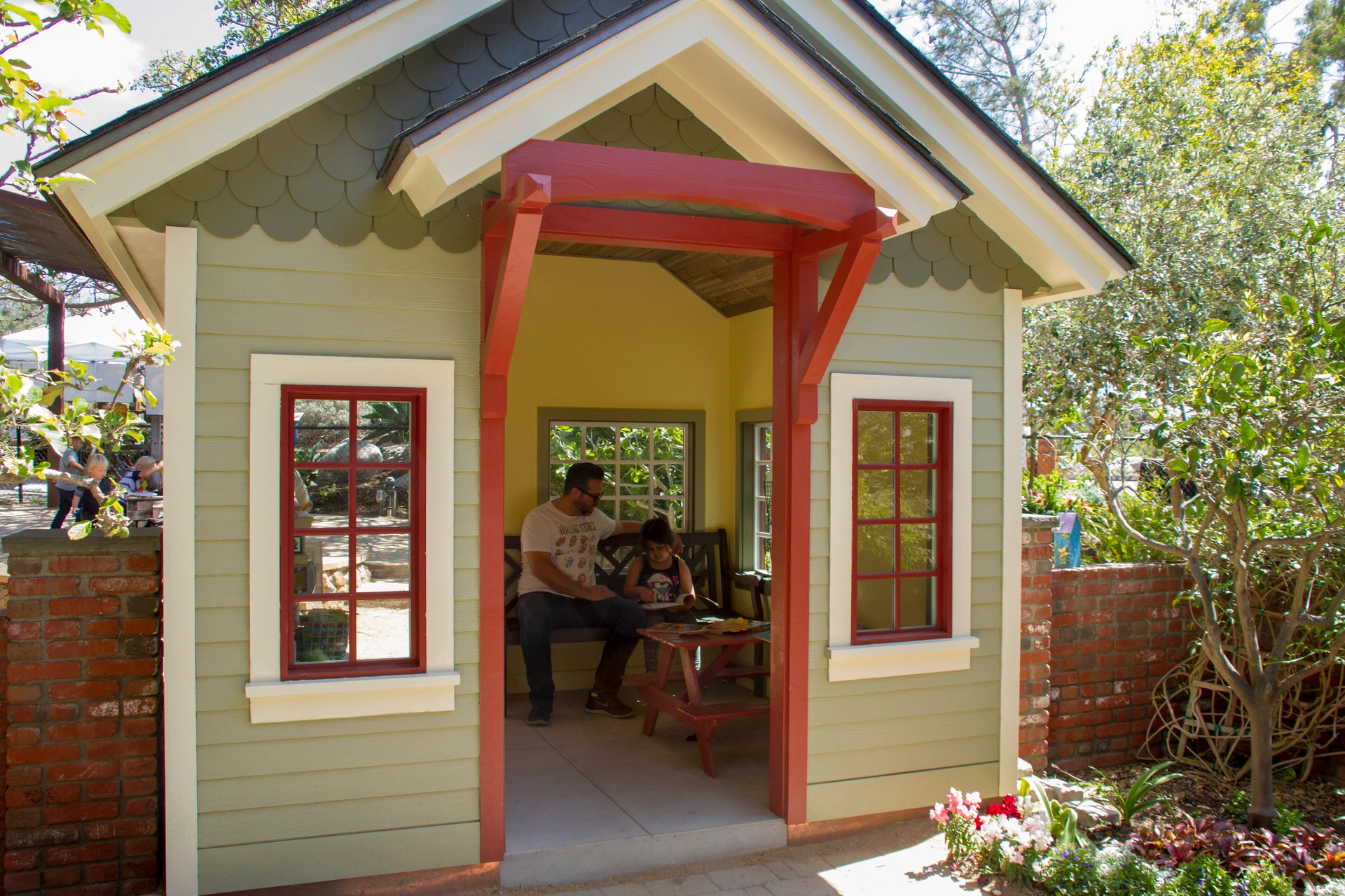 A man and girl sit on a bench inside the Seeds of Wonder playhouse.
