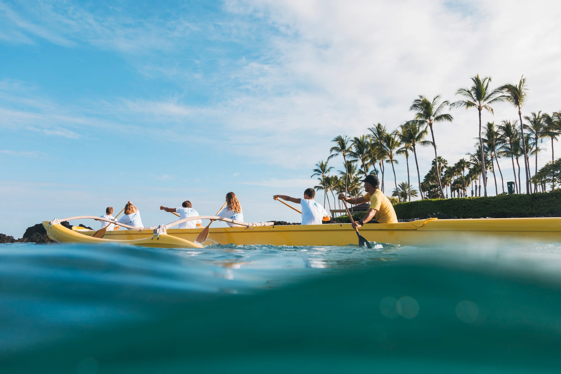 Guests paddle an outrigger canoe in front of Four Seasons Hualalai